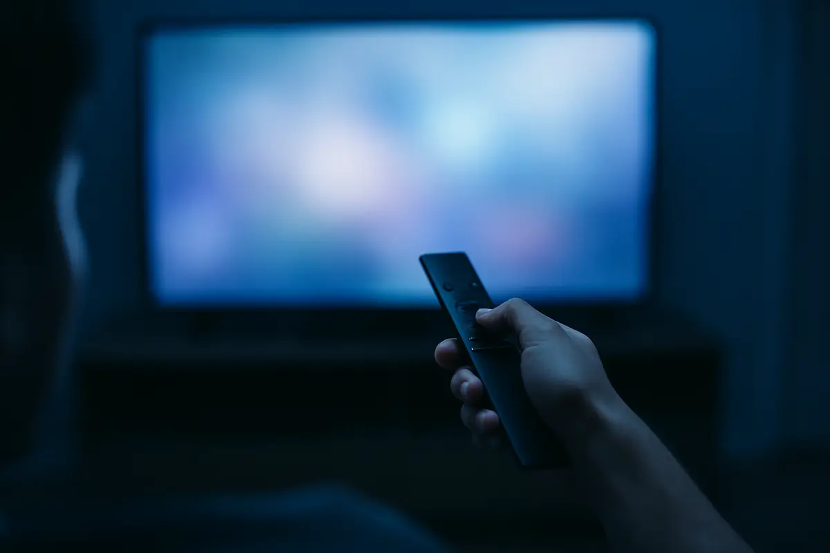 A hand pressing a button on a TV remote in a dim room, as when cold-restarting a smart TV.